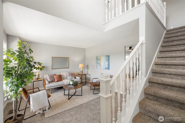 living room featuring stairs, carpet flooring, baseboards, and a high ceiling
