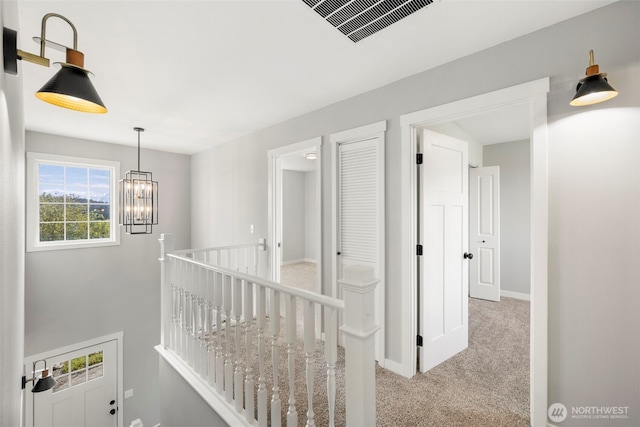 hallway with an upstairs landing, carpet floors, a chandelier, and baseboards