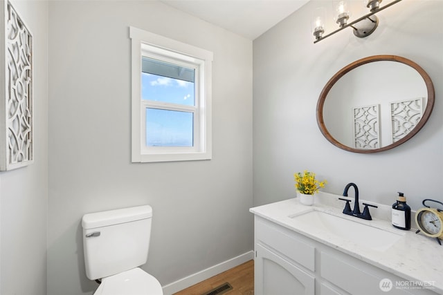 half bathroom with wood finished floors, baseboards, toilet, and vanity