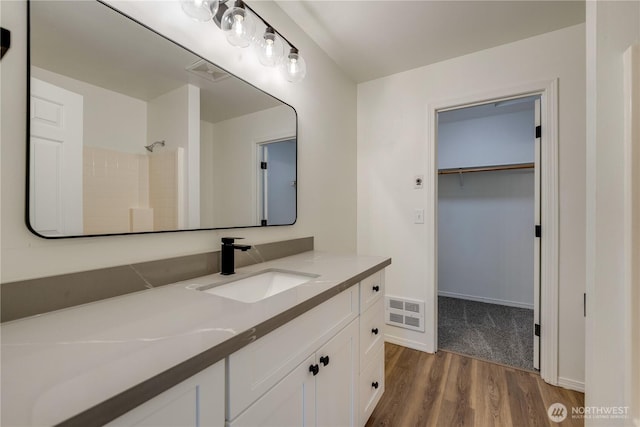 full bathroom with visible vents, vanity, a shower, wood finished floors, and a walk in closet