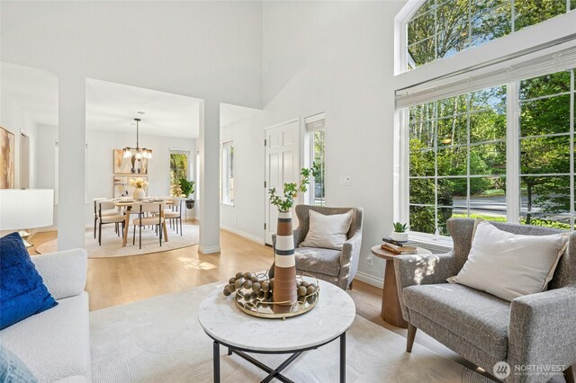 living room with a high ceiling, a notable chandelier, baseboards, and light wood finished floors