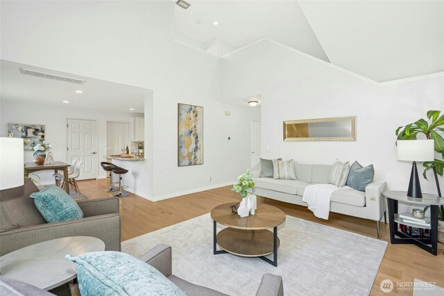 living area featuring high vaulted ceiling, visible vents, baseboards, and light wood-style floors