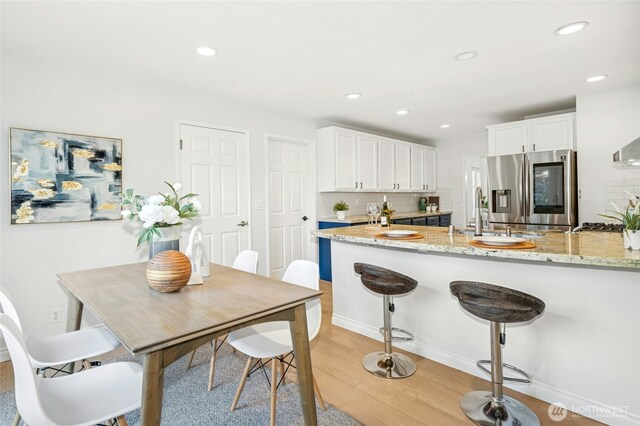 kitchen with a sink, light wood finished floors, white cabinets, and stainless steel fridge with ice dispenser