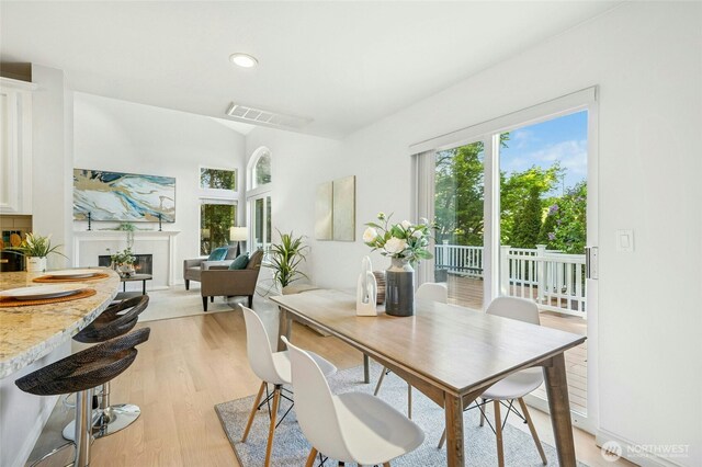 dining area featuring light wood-style flooring, a glass covered fireplace, a wealth of natural light, and visible vents