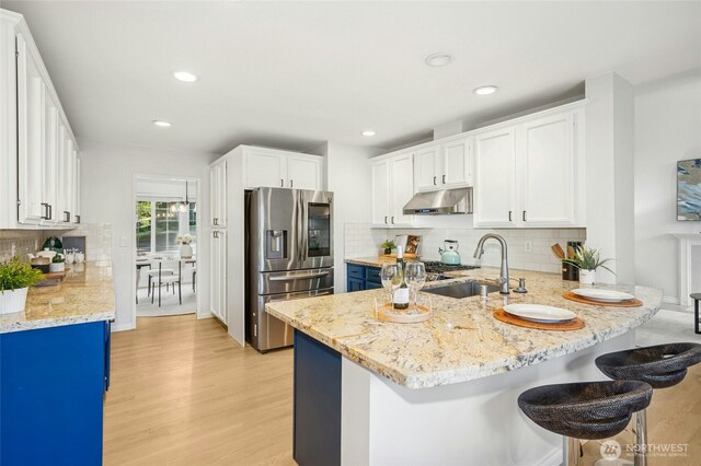 kitchen featuring a peninsula, light wood-style floors, stainless steel refrigerator with ice dispenser, under cabinet range hood, and a sink