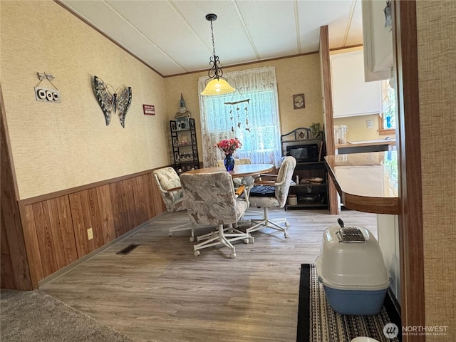 dining space with wooden walls, a wainscoted wall, wood finished floors, visible vents, and ornamental molding