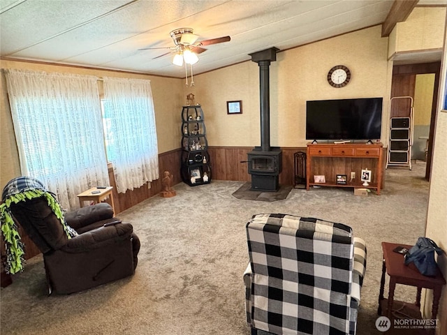 carpeted living area with wood walls, a wood stove, lofted ceiling, a wainscoted wall, and a ceiling fan