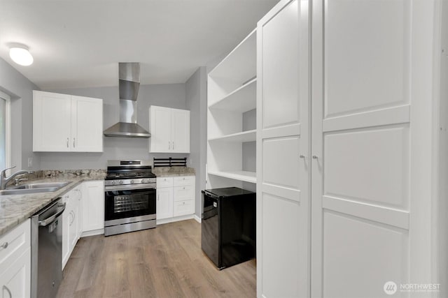 kitchen featuring appliances with stainless steel finishes, a sink, wall chimney exhaust hood, open shelves, and light wood finished floors