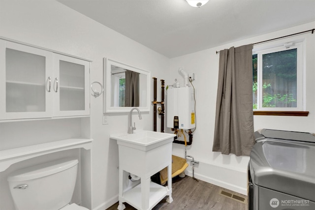 bathroom with washing machine and dryer, toilet, water heater, and wood finished floors