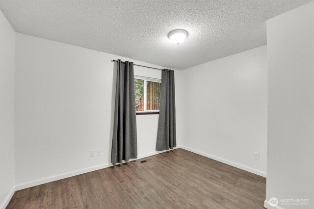 empty room featuring wood finished floors, a textured ceiling, and baseboards