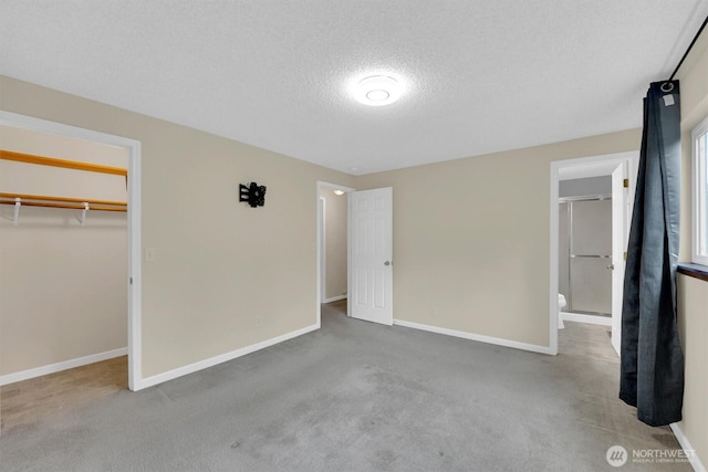 unfurnished bedroom featuring a textured ceiling, carpet, baseboards, a spacious closet, and a closet