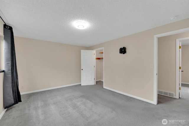 carpeted empty room featuring a textured ceiling, baseboards, and a smoke detector