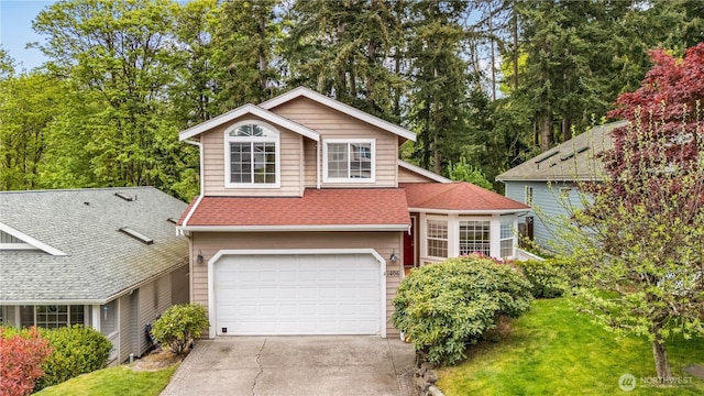 tri-level home featuring a shingled roof, an attached garage, concrete driveway, and a front yard