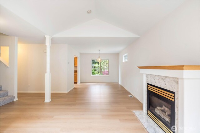 unfurnished living room with a fireplace, baseboards, light wood finished floors, lofted ceiling, and stairs