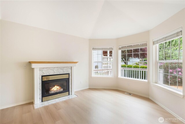 unfurnished living room with baseboards, visible vents, wood finished floors, and a high end fireplace
