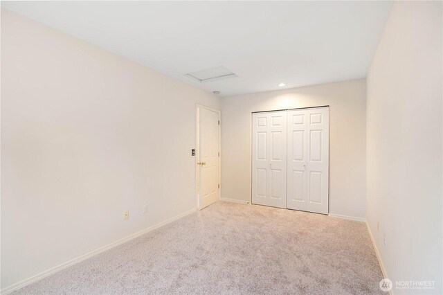 unfurnished bedroom featuring carpet floors, baseboards, attic access, and a closet
