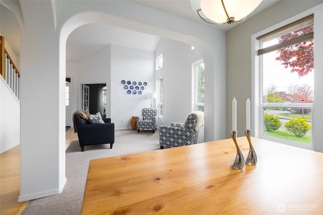 dining area featuring arched walkways, carpet, vaulted ceiling, and stairs