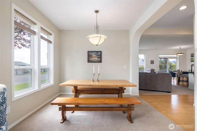 dining area with arched walkways, baseboards, and light wood-style floors
