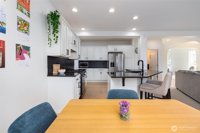 kitchen with dark countertops, appliances with stainless steel finishes, a sink, arched walkways, and open floor plan