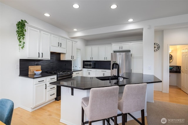 kitchen featuring dark countertops, a sink, a breakfast bar, stainless steel appliances, and white cabinetry