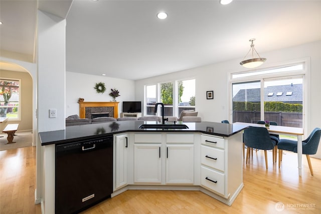 kitchen with dark countertops, dishwasher, a sink, open floor plan, and light wood-style flooring