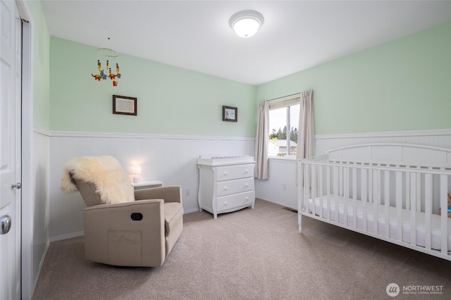 carpeted bedroom featuring wainscoting and a crib