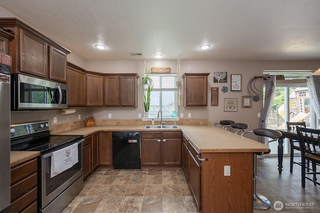 kitchen with a sink, stainless steel appliances, a peninsula, a kitchen bar, and visible vents
