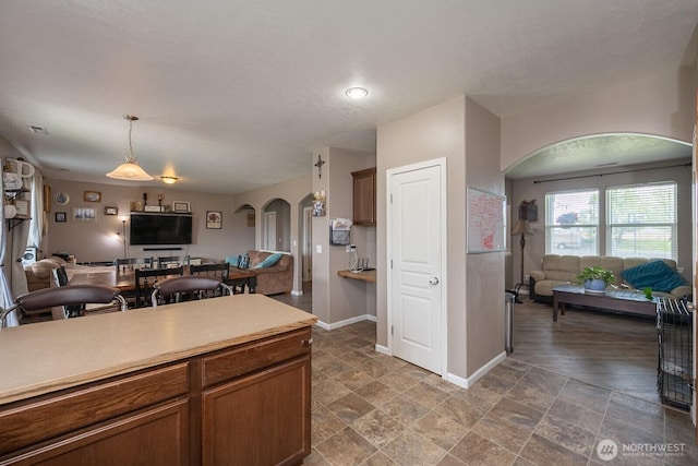 kitchen featuring baseboards, open floor plan, light countertops, arched walkways, and decorative light fixtures