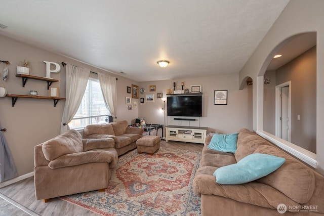 living room featuring visible vents, arched walkways, baseboards, and wood finished floors