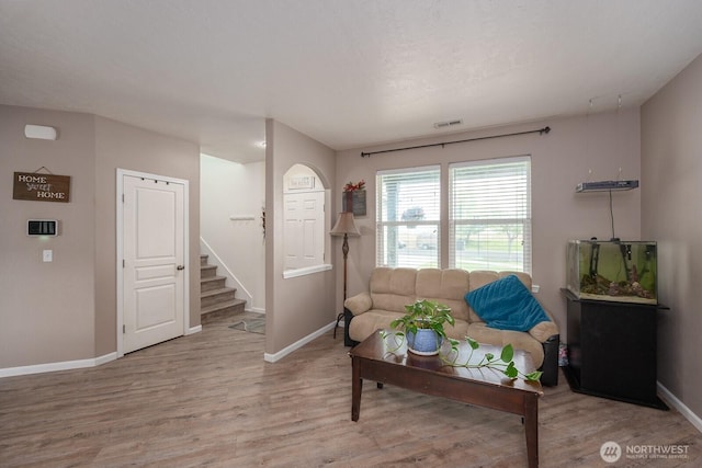 living room featuring baseboards, visible vents, wood finished floors, and stairway
