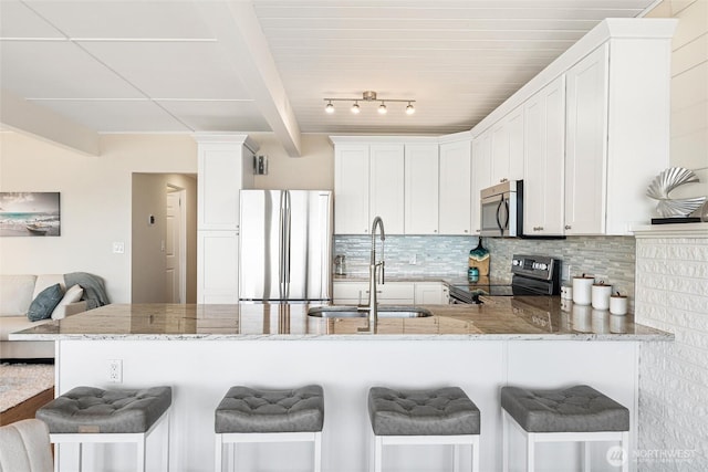 kitchen with light stone countertops, appliances with stainless steel finishes, a sink, a peninsula, and backsplash