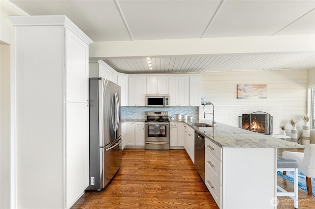 kitchen with appliances with stainless steel finishes, a sink, light stone counters, a peninsula, and white cabinetry