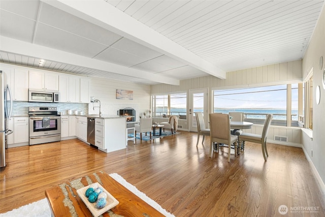 dining room featuring a brick fireplace, beamed ceiling, visible vents, and light wood-style floors