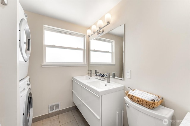 bathroom featuring visible vents, tile patterned flooring, a sink, toilet, and stacked washer and clothes dryer