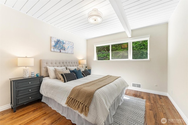 bedroom with visible vents, baseboards, wood finished floors, and beam ceiling