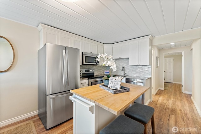 kitchen featuring decorative backsplash, a kitchen breakfast bar, wooden counters, stainless steel appliances, and white cabinetry