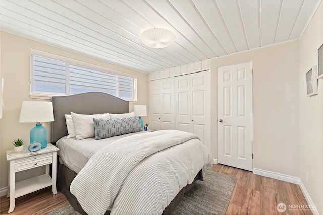 bedroom featuring a closet, baseboards, wood finished floors, and wood ceiling