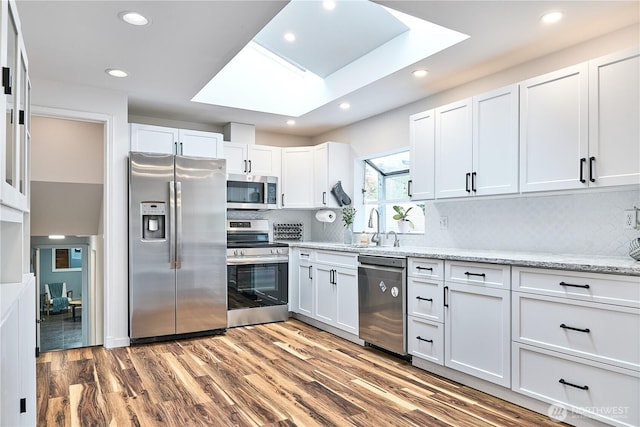15722 62nd Pl NE, Kenmore, WA 98028 - kitchen featuring appliances with stainless steel finishes, a skylight, white cabinets, tasteful backsplash, and wood finished floors