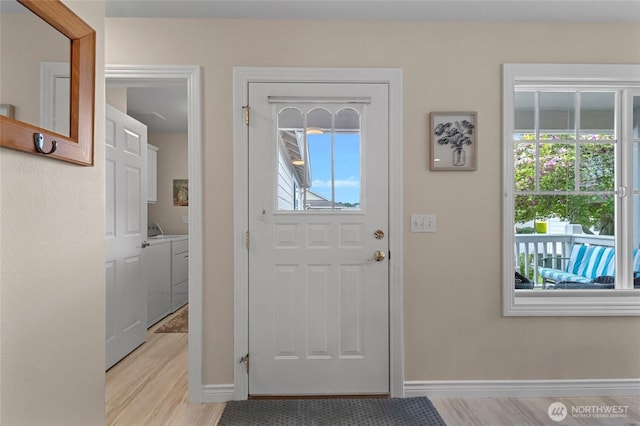 foyer featuring independent washer and dryer, baseboards, and light wood-style flooring