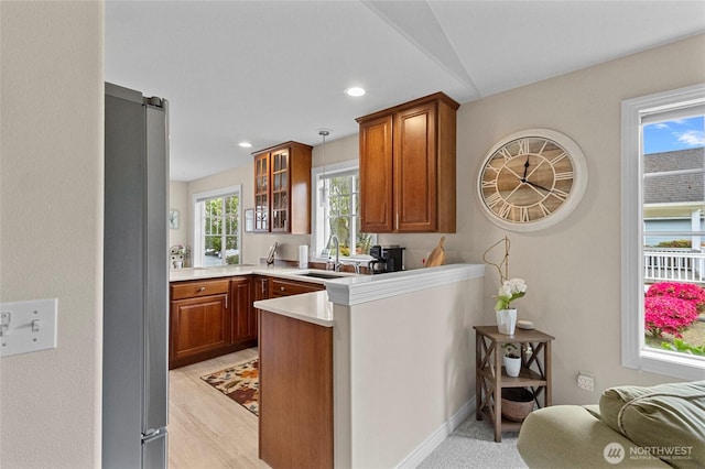 kitchen featuring brown cabinetry, freestanding refrigerator, a peninsula, glass insert cabinets, and a sink