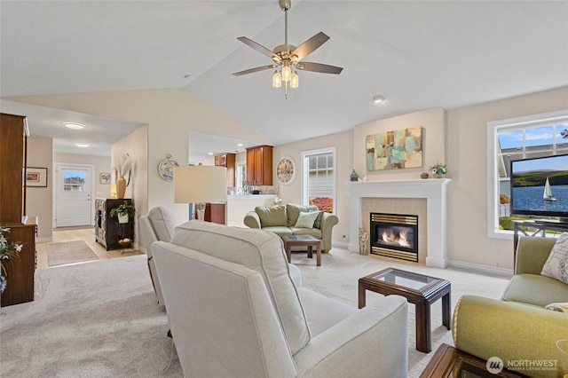living area with baseboards, light colored carpet, a tiled fireplace, a ceiling fan, and vaulted ceiling