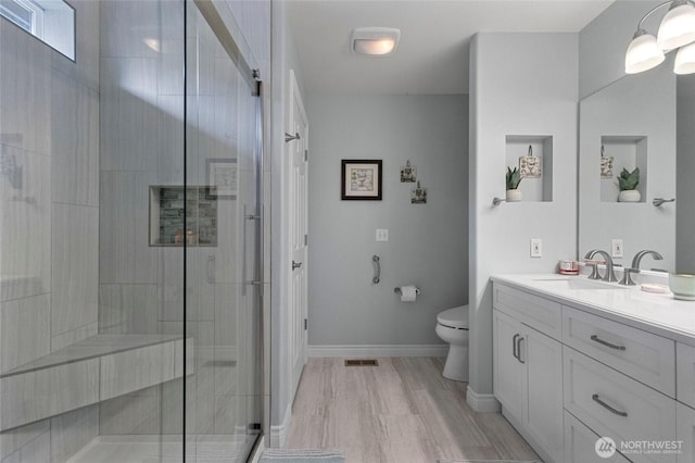 bathroom with vanity, visible vents, toilet, baseboards, and a shower stall