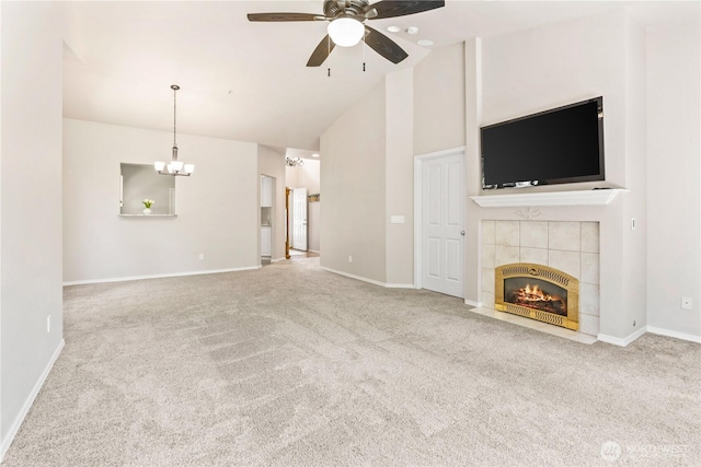 unfurnished living room with carpet flooring, a tile fireplace, ceiling fan with notable chandelier, high vaulted ceiling, and baseboards