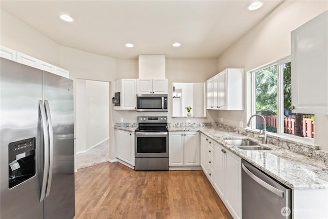 kitchen featuring light stone counters, a sink, wood finished floors, white cabinets, and appliances with stainless steel finishes