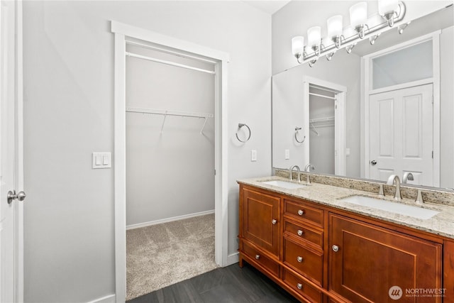 bathroom with a sink, a walk in closet, double vanity, and baseboards