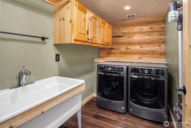 clothes washing area with visible vents, washing machine and clothes dryer, cabinet space, a sink, and dark wood-style floors