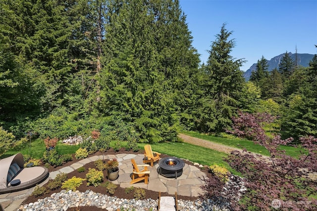 view of yard featuring a mountain view, an outdoor fire pit, a patio area, and a wooded view