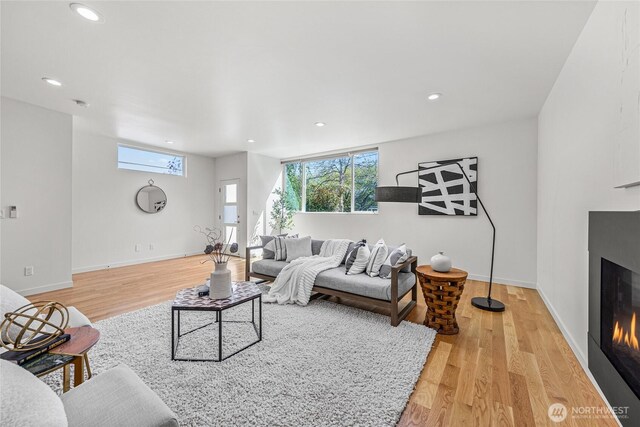 living room with recessed lighting, a glass covered fireplace, light wood finished floors, and a wealth of natural light