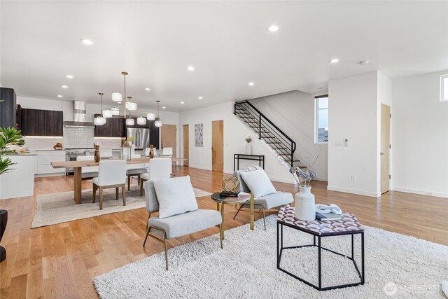living area featuring stairs, recessed lighting, plenty of natural light, light wood finished floors, and a notable chandelier