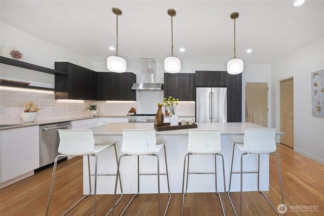 kitchen featuring wall chimney range hood, tasteful backsplash, open shelves, light countertops, and stainless steel appliances